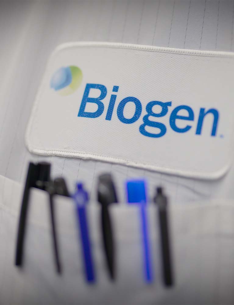 Gros plan sur une blouse blanche et une veste Biogen avec plusieurs stylos dans une poche